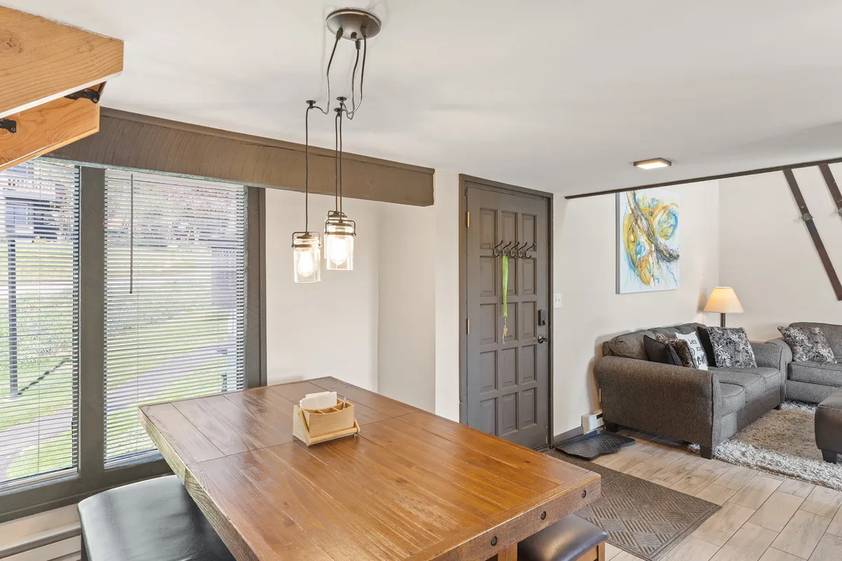 A cozy dining area is depicted, featuring a spacious dining table set for gatherings, with a comfortable sofa and artwork visible in the background. The setup invites guests to share meals, socialize, and create memories in a warm, homey environment.