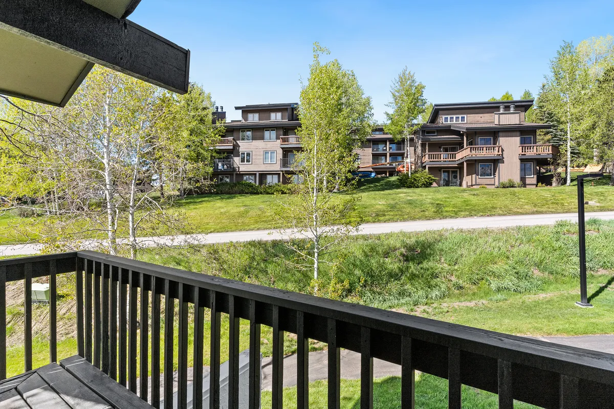 The photo showcases a balcony with a sturdy railing overlooking trees and nearby buildings. The view hints at the tranquility of the surrounding area and the opportunity to enjoy fresh mountain air. It also subtly connects to outdoor socializing and scenic outdoor living.
