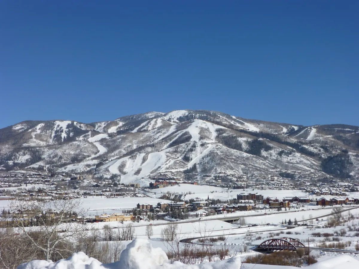 A sweeping view of snow-covered mountains, active ski slopes, a river winding through the valley, and the town below. The invigorating scene highlights Steamboat’s winter playground and hints at the variety of activities available, from skiing to exploring the local area.