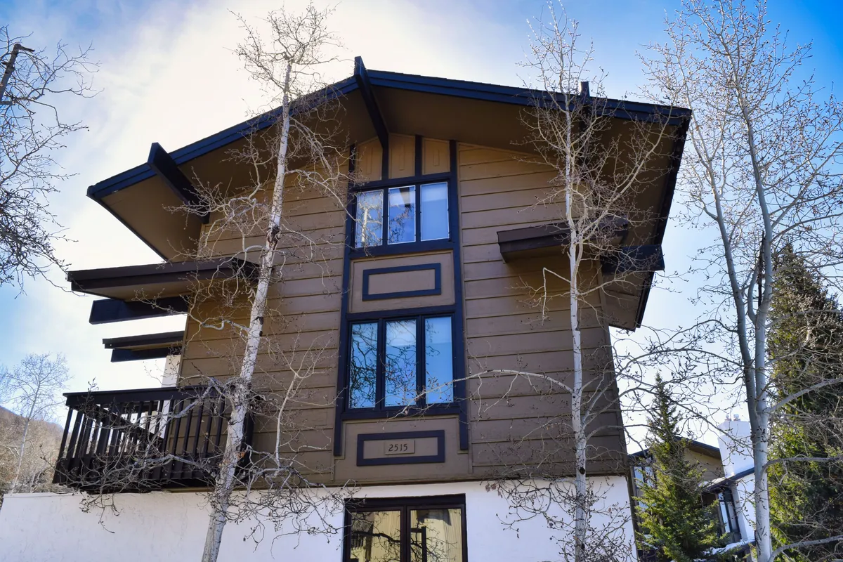 The image focuses on the building facade, large windows, and a welcoming balcony. The setting suggests moments where couples can enjoy coffee in the morning or unwind together after a day of exploring the town. The presence of the balcony and large windows alludes to indoor-outdoor living, enhancing the sense of connection to Steamboat’s charming environment.