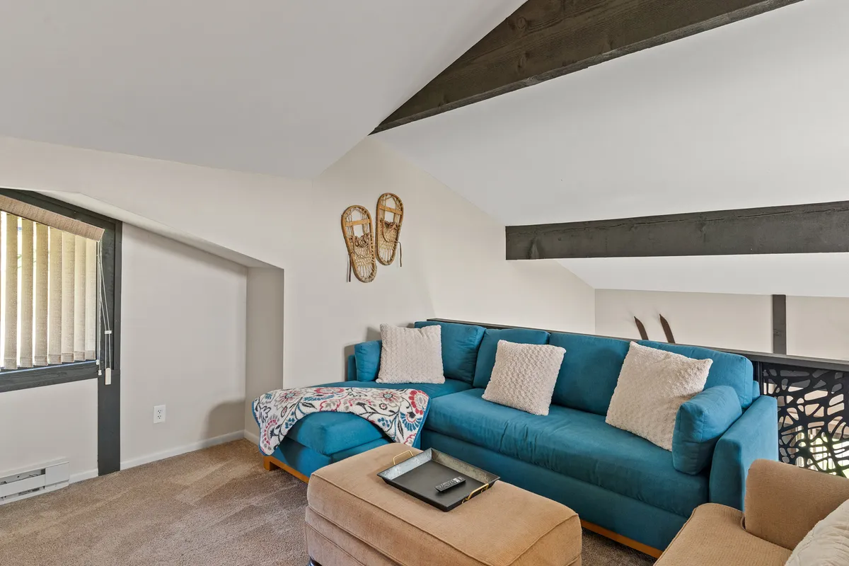 This image features a welcoming living area anchored by a blue sectional sofa, accented with decorative snowshoes and a textured throw blanket. A coffee table sits nearby, with a window flooding the space with natural light, suggesting a cozy spot for family gatherings after outdoor adventures.