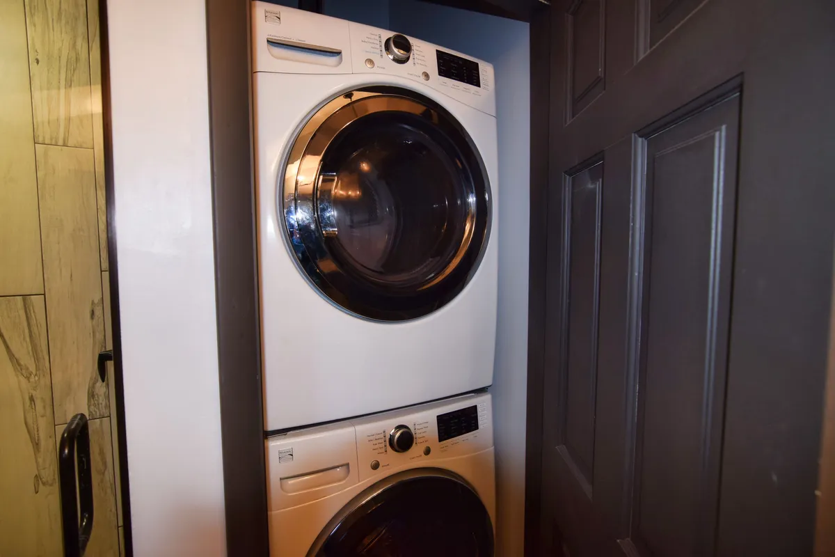 A stacked washer and dryer are neatly tucked into a corner, framed by a doorway. The space is clean and organized, ready for families needing to refresh their clothes after outdoor fun.