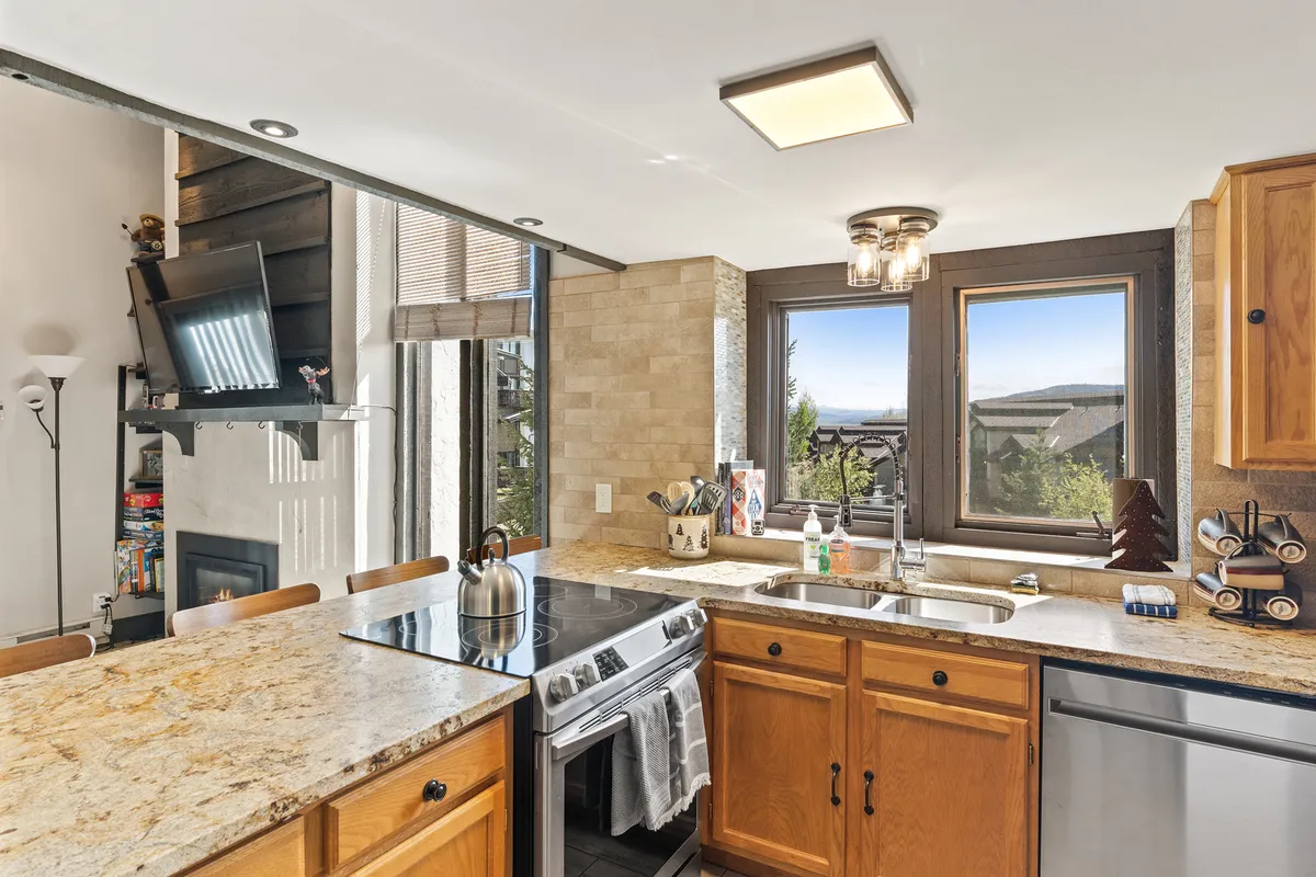 This image features a modern kitchen with gleaming granite countertops, stainless steel appliances, and a window that brings in natural light and offers scenic views. The layout suggests ample space for cooking and socializing, with all major appliances visible and ready for use.